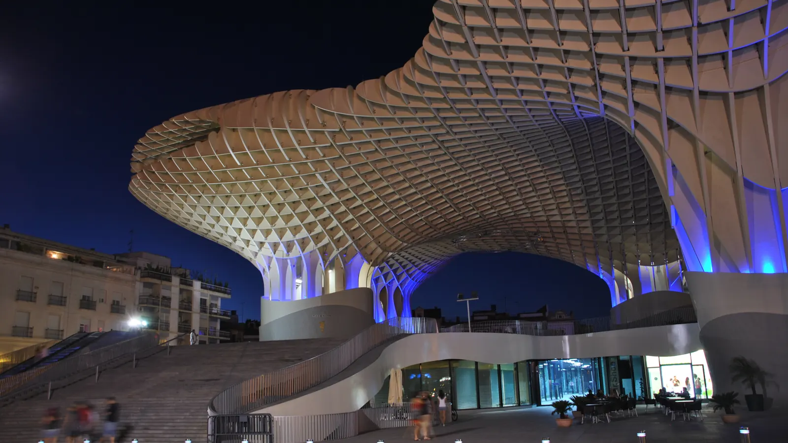 Metropol Parasol om natten, hvor dens tømmergitter lyser op over den glaserede stueetage og de brede trapper på Plaza de la Encarnación