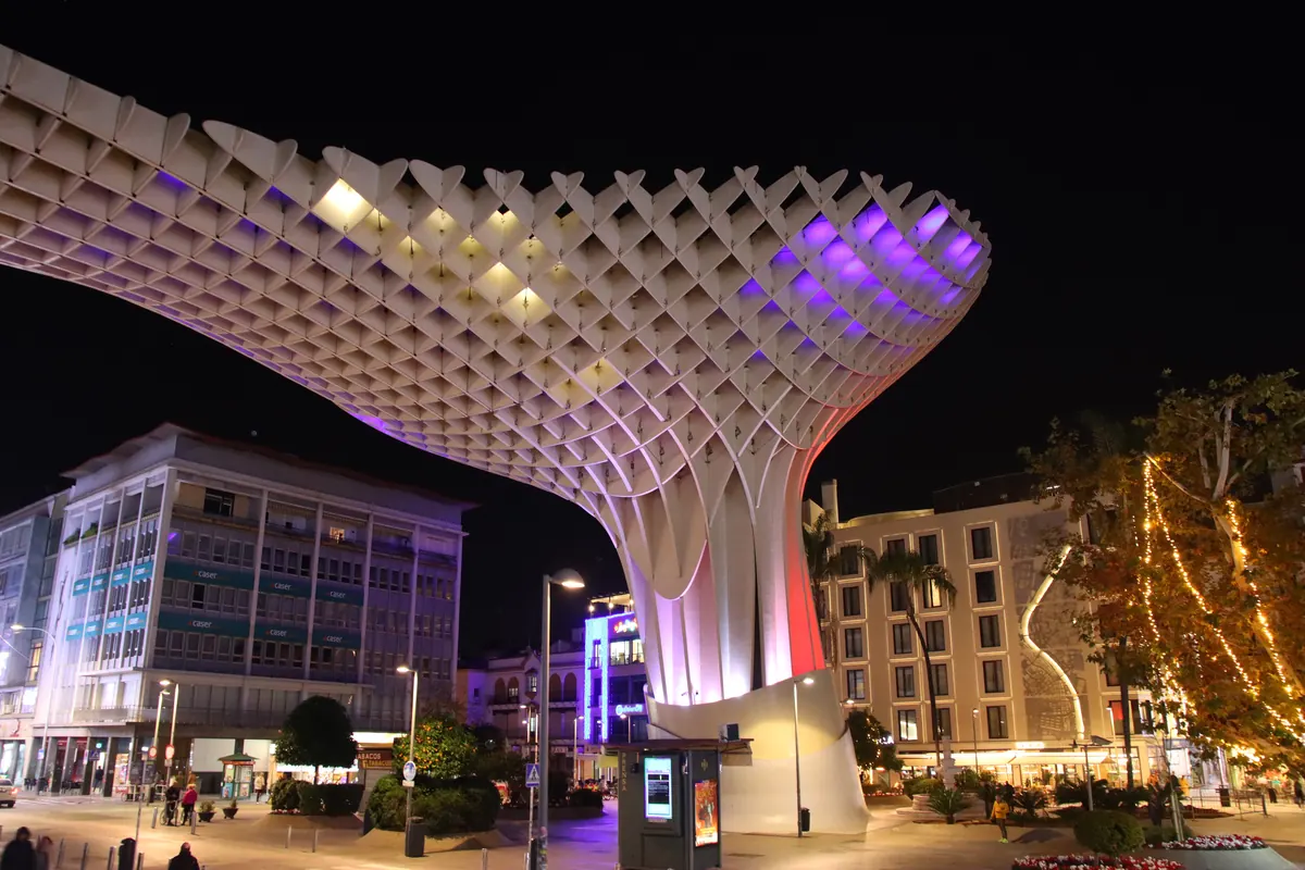 Metropol Parasol v Seville v noci, jeho světlá dřevěná mříž nad Plaza de la Encarnación zářící fialovou a zlatou
